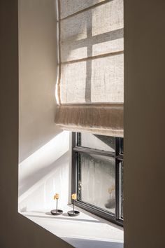 an open window in a white room next to a small vase with flowers on it