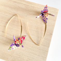 pair of earrings with origami cranes on them sitting on wooden board next to white background