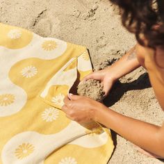 a woman is sitting on the beach with her hand on a towel that has been folded over it