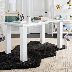 a white dining table with clear chairs in front of it and an area rug on the floor