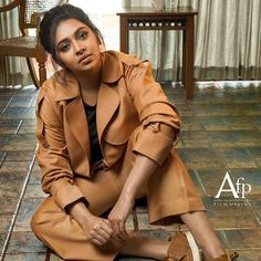 a woman is sitting on the floor in a tan coat and brown shoes with her legs crossed