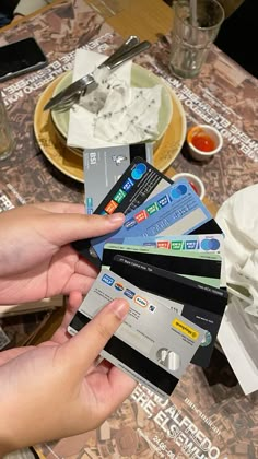 a person holding four credit cards in front of a table with plates and silverware on it