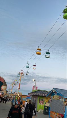 many people are walking down the street in front of some shops and carnival rides at dusk