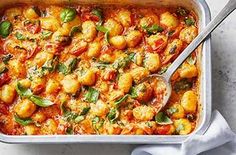 a casserole dish filled with chicken, tomatoes and spinach garnished with basil