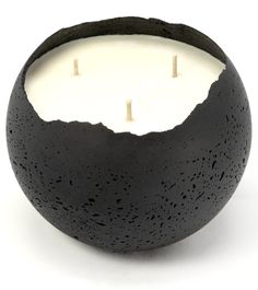 a candle that is inside of a black bowl on a white surface with three candles in it