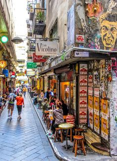 people are walking down an alleyway with shops and restaurants on either side, in the city