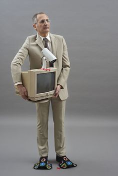 a man in a suit and tie holding a computer monitor with a microphone attached to it