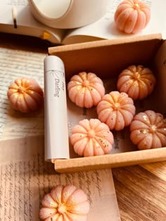 some small oranges are in a box on a table next to an open book