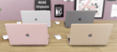 three apple laptops sitting on top of a wooden table