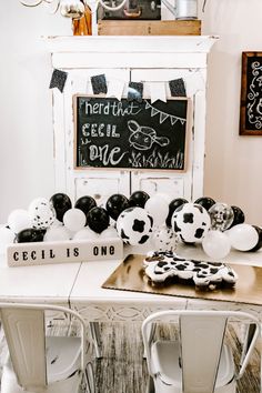 a white table topped with lots of black and white balloons in front of a chalkboard