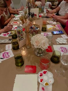 a group of people sitting around a table with paint and paper on it, surrounded by cards