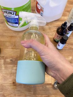 a person holding a bottle with liquid in it on top of a wooden table next to other bottles