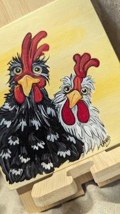 a painting of two roosters on a wooden block with yellow background and wood frame