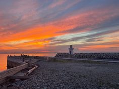 a light house sitting on top of a rocky beach next to the ocean at sunset