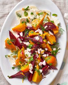 a white plate topped with sliced beets and feta cheese covered in fresh herbs