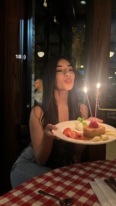 a woman sitting at a table holding a plate with food on it and lit candles