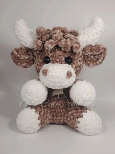 a brown and white stuffed cow sitting on top of a gray surface with its eyes wide open