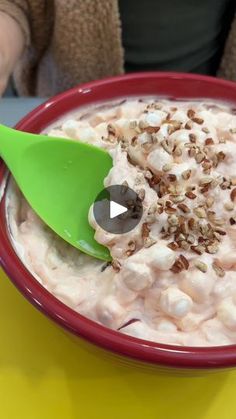 a red bowl filled with food on top of a yellow table next to a green spoon