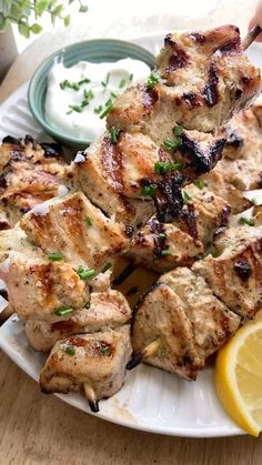 a white plate topped with chicken and lemon wedges next to a bowl of ranch dressing