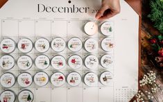 a person is holding a lit candle next to a calendar with christmas decorations on it