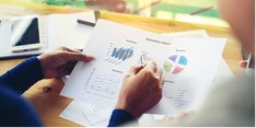 two people sitting at a table with papers and pens in front of them, looking at graphs