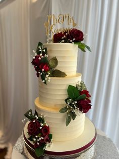 a three tiered wedding cake with red roses and greenery