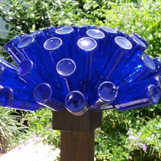 a blue glass fan sitting on top of a wooden post in front of some bushes