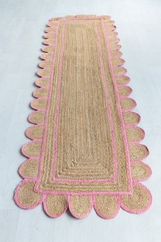 a pink and beige rug with scalloped edges on a white floor in an empty room