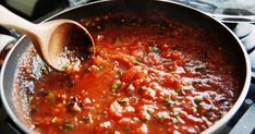 a wooden spoon in a pot filled with tomato sauce