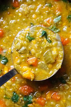 a ladle full of soup with carrots, corn and spinach in it