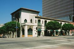 an empty street in front of a building with trees on the corner and tall buildings behind it