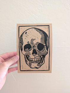 a hand holding up a piece of paper with a drawing of a skull on it