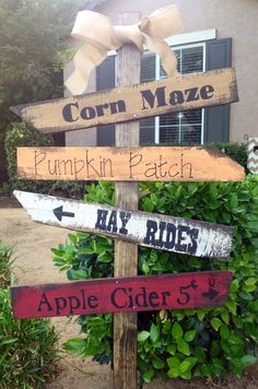 a wooden sign that has some signs on it in front of a house and bushes