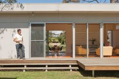 a man standing on the porch of a house with sliding glass doors and wooden decking