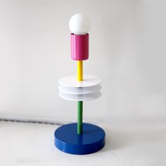 a multicolored object is standing on a blue base with a white ball in the middle