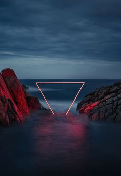 an image of a triangle in the water with rocks and red light coming from it