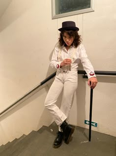 a woman in white pants and top hat leaning against a wall with a cane on the ground