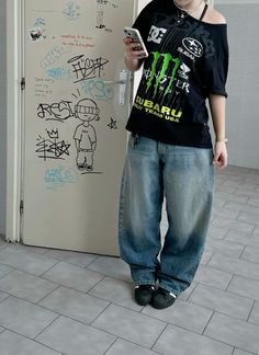 a young man standing in front of a white wall with graffiti on it and looking at his cell phone