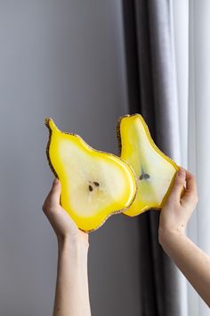 a person holding a piece of fruit in front of a window with curtains behind it