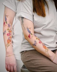 a woman with flowers on her arm is sitting down and has tattoos on her arms