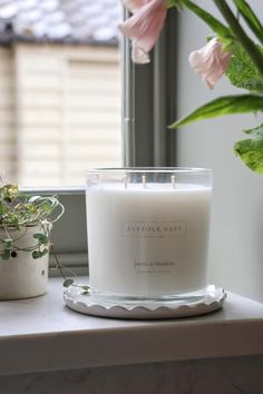 a white candle sitting on top of a table next to a potted plant