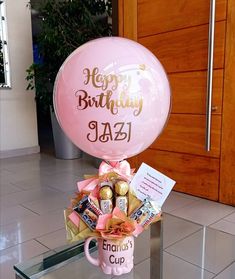 a pink birthday balloon with chocolates and candies in it sitting on top of a glass table