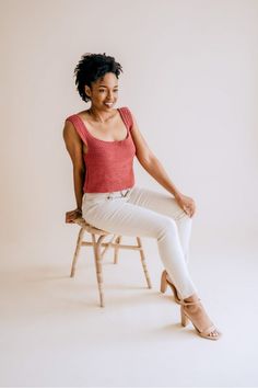 a woman sitting on top of a wooden chair wearing white pants and a red shirt