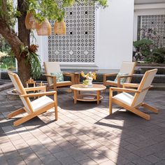 a group of wooden chairs sitting on top of a brick floor next to a tree