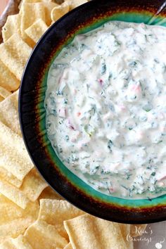 a black bowl filled with white dip surrounded by tortilla chips