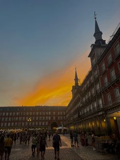 people are walking around in an old town square at sunset or dawn with the sun going down