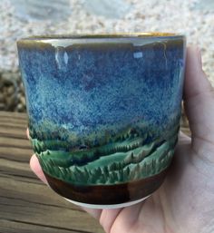 a hand holding a blue and green cup