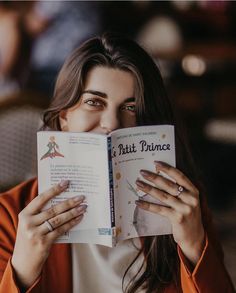 a woman reading a book with her hands on her face and looking at the camera