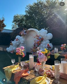 a table with flowers and candles on it in front of an outdoor backdrop that looks like clouds