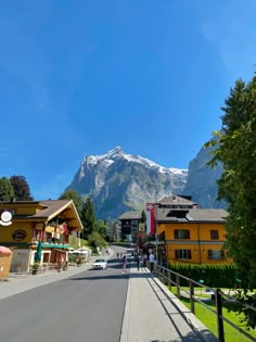 people are walking down the street in front of some buildings with mountains in the background